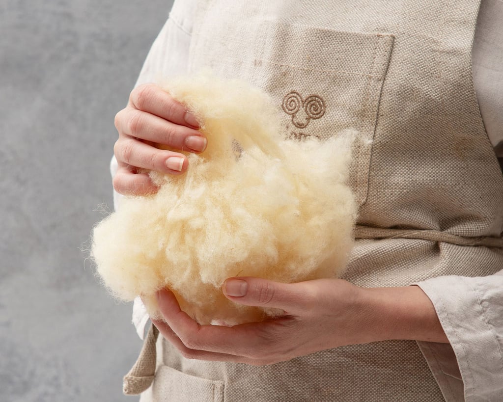 Person in a beige apron holding a bundle of loose cream wool.