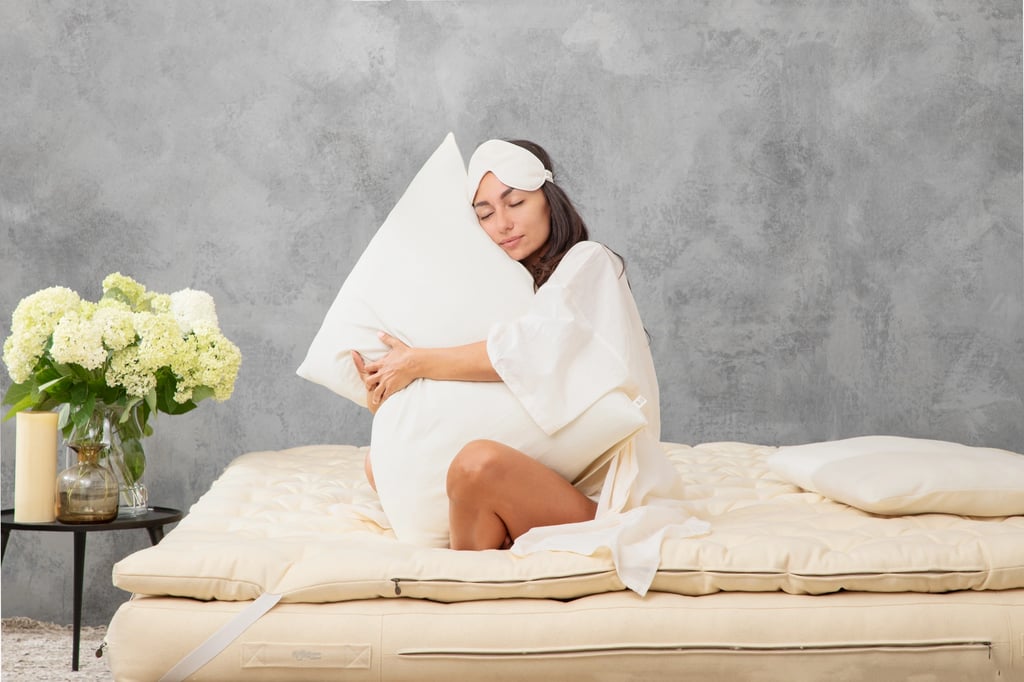 Woman in profile hugging a home of wool pillow while sitting on home of wool mattress. Flowers in the background.