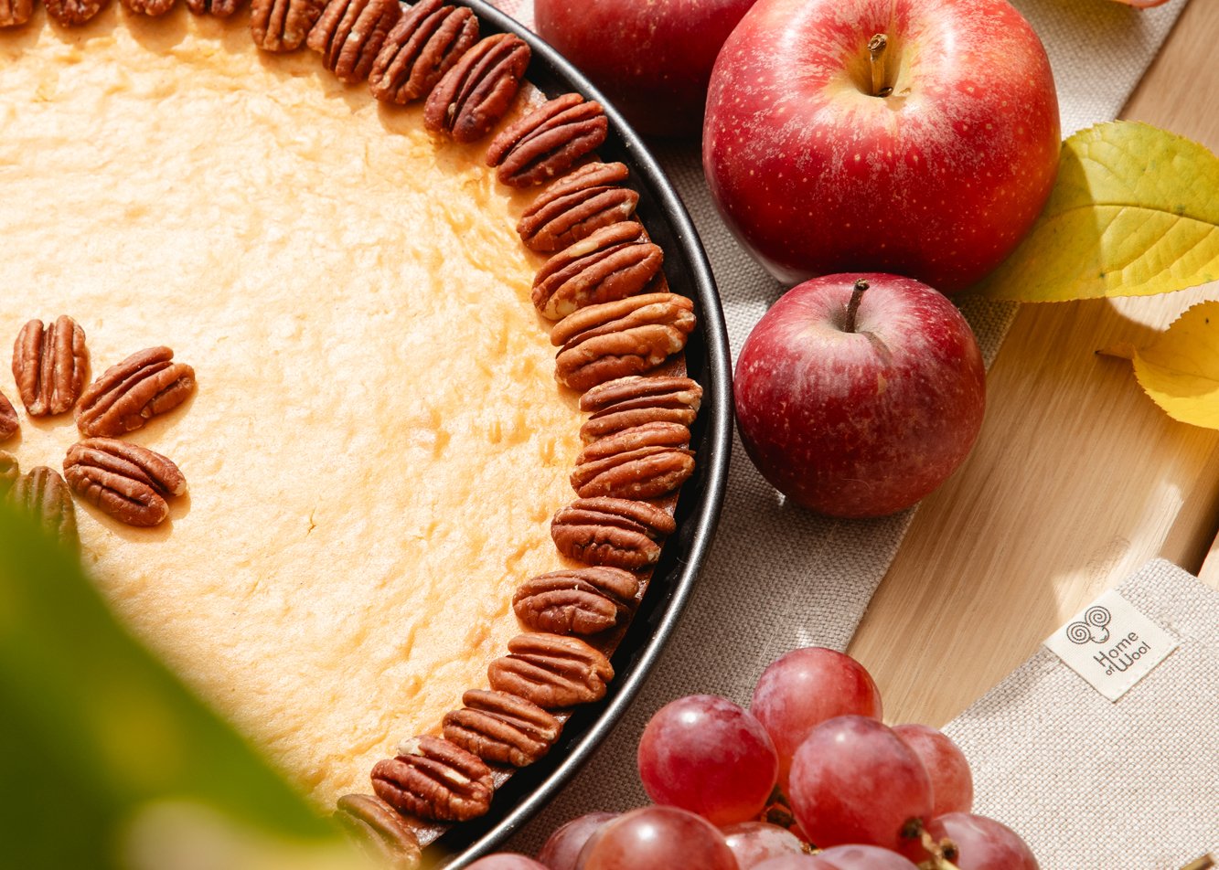 Pie decorated with pecans beside red apples, grapes and autumn leaves.