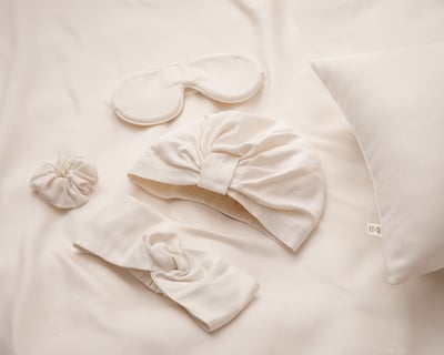 Maschera per il sonno, turbante, scrunchie e fascia per capelli posati su una superficie di seta