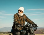 man with sunglasses on a motorcycle with nomad heat beanie and neck gaiter with sky in the background