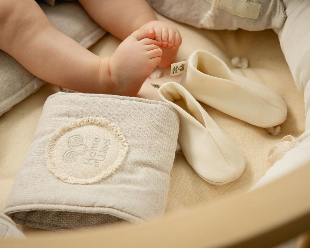 Babyfüße neben weichen Babyschuhen aus Merinowolle auf einer kuscheligen Stoffoberfläche