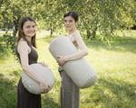 Two girls holding a zafu cushion and a bolster pillow for yoga in the park