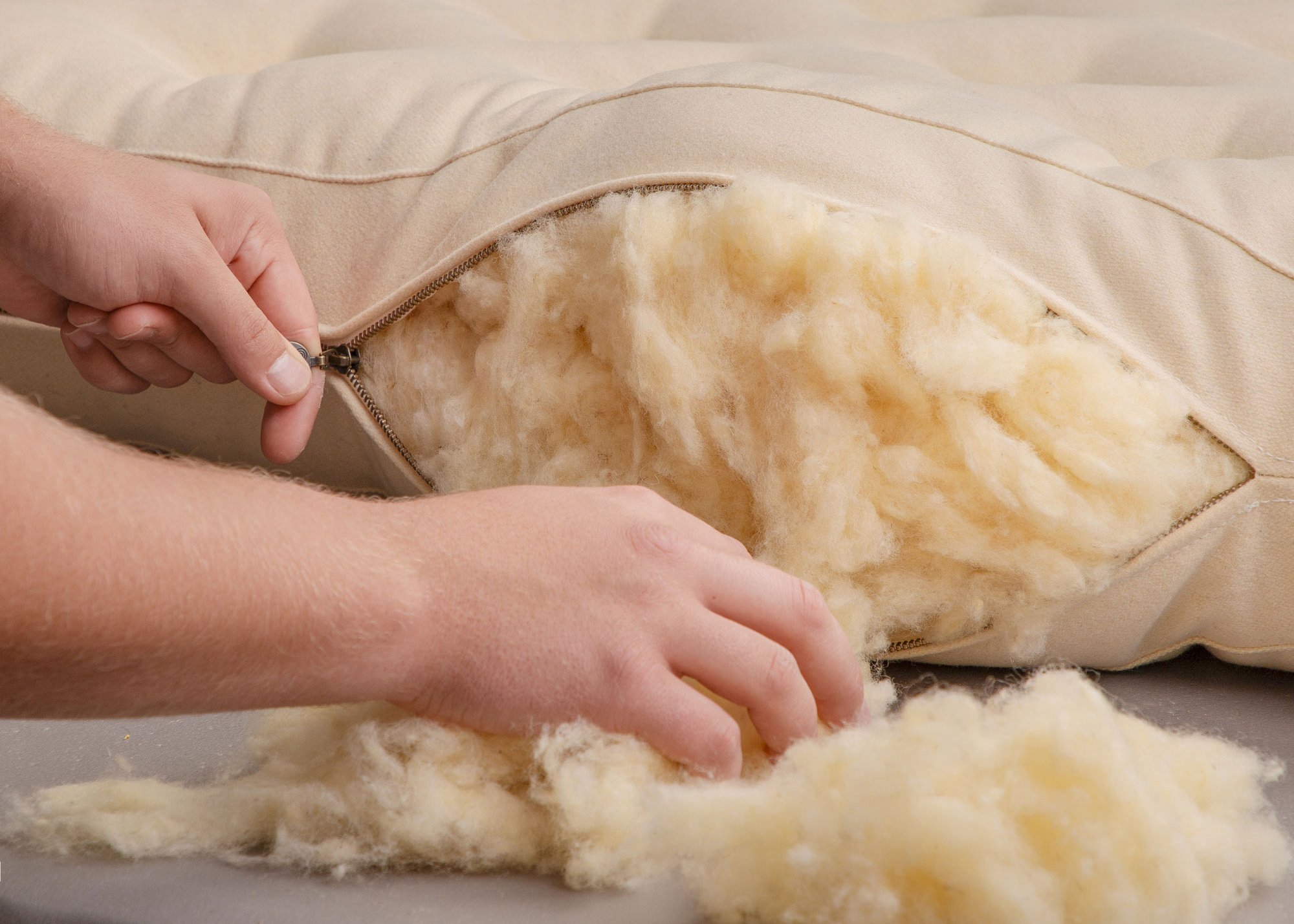 Hands opening a cream fabric cover to reveal loose wool filling.