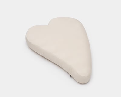 A heart-shaped wool pillow with a soft cotton cover in a light neutral color, designed for comfort with a simple, minimalist look.